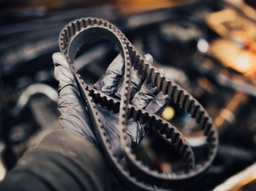 Paskirstymo diržas mechaniko rankoje automobilio variklio fone