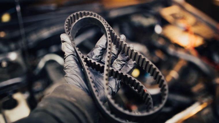 Paskirstymo diržas mechaniko rankoje automobilio variklio fone