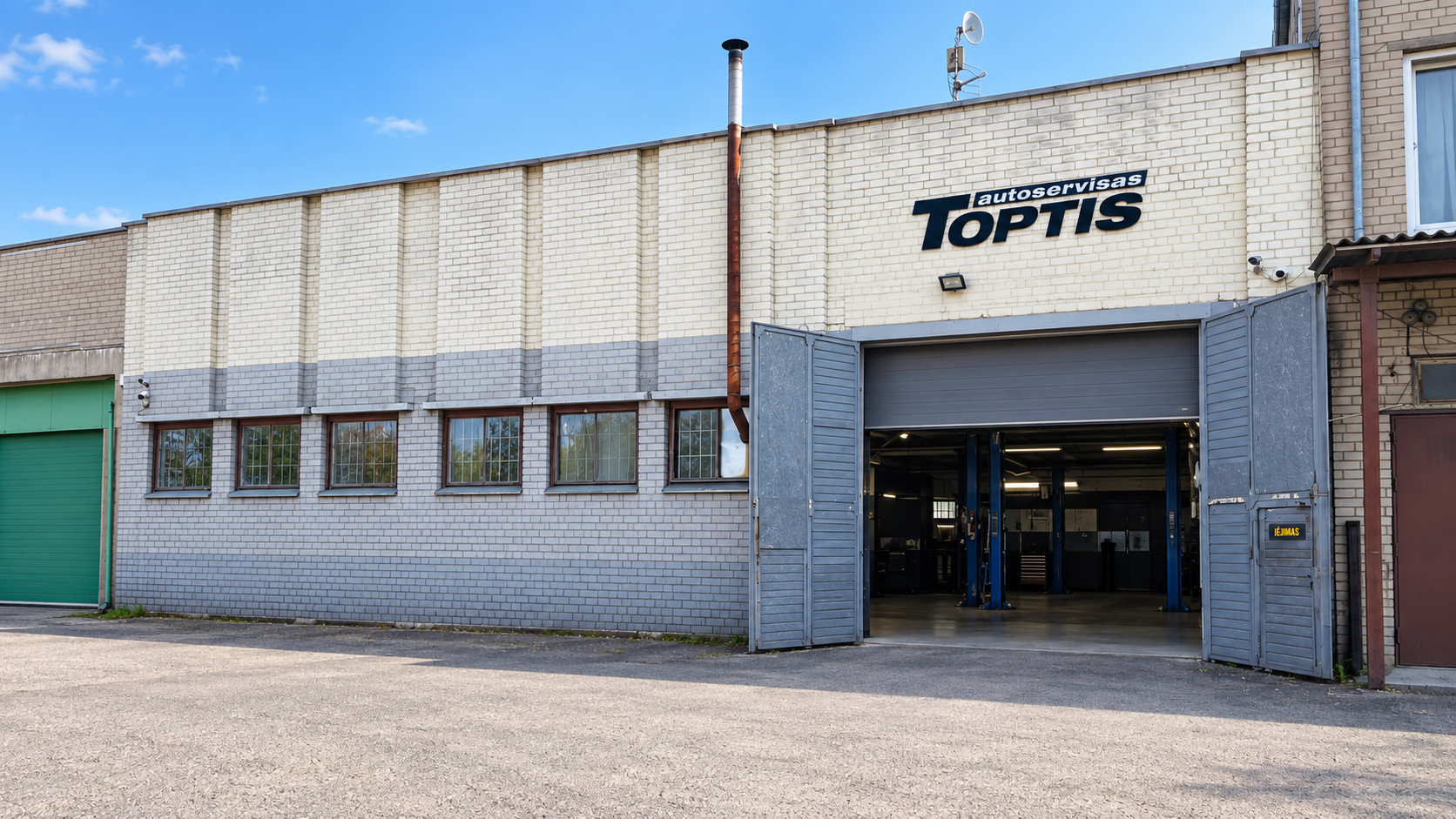 Toptis autoservisas Verkių g. 50 – šviesus plytų pastatas su iškaba, atviru garažo vartų angos ir pilkais vartais