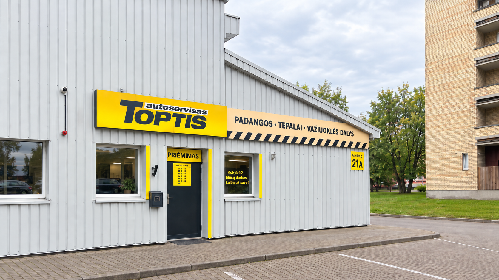 Toptis autoservisas Ateities g. 21A – pilkas pastatas su geltona iškaba ir priėmimo durimis